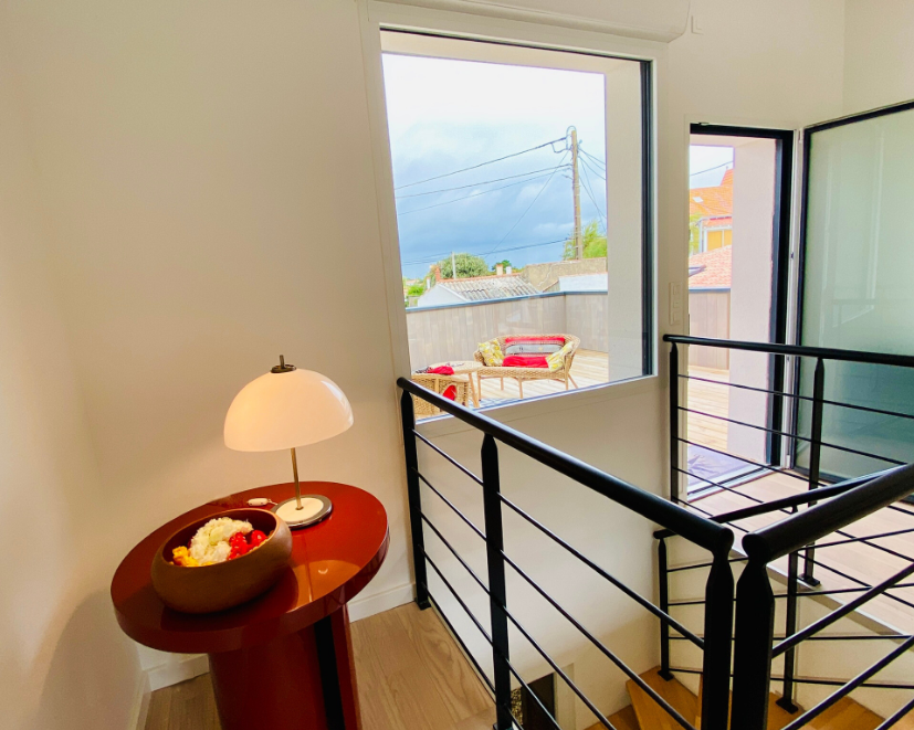 Un coin cosy avec une petite table vintage, une lampe et un aperçu d'un balcon avec des sièges par la fenêtre.
